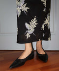 Person wearing a black floral embroidered skirt and black shoes on a wooden floor.