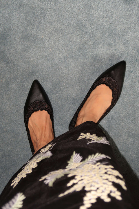 Black pointed-toe shoes with lace details worn with a black kebaya kurung  with white floral embroidery.