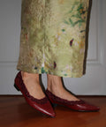 Person wearing a green floral skirt and red shoes on a wooden floor.