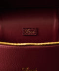 Close-up of a burgundy handbag with gold zipper and visible brand logo.